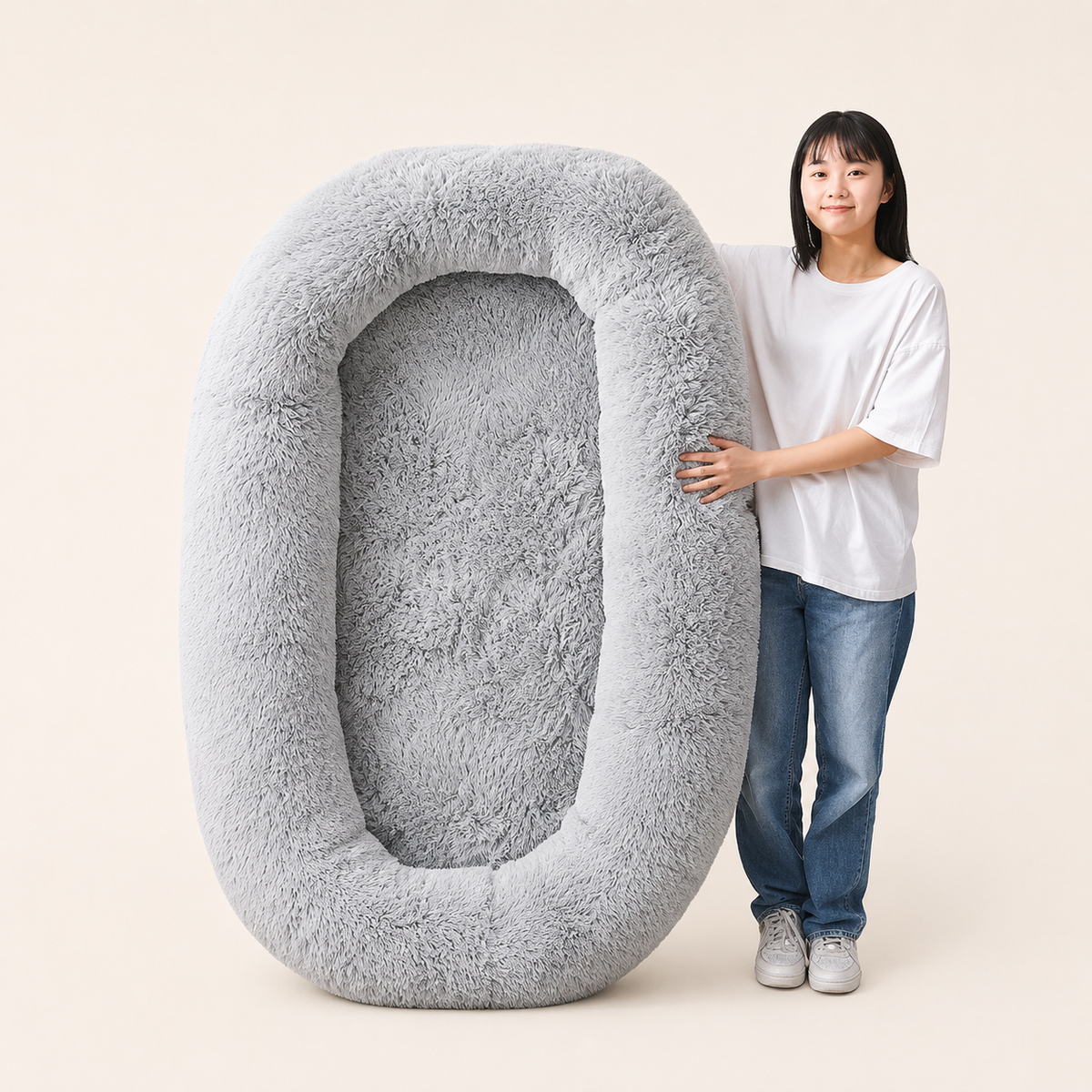 Adult standing beside the grey Human Dog Bed, showing its full size