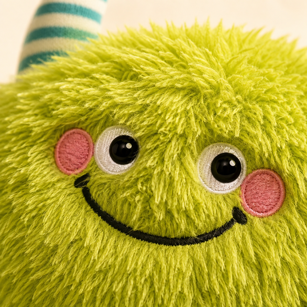 Close-up of the Monster Nest Bed embroidered face and striped horn on green plush